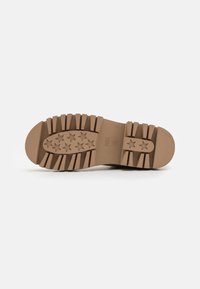 Suela de zapato de goma marrón con surcos prominentes, que presenta patrones en forma de estrella y una parte delantera redondeada. Superficie texturizada para un mejor agarre.