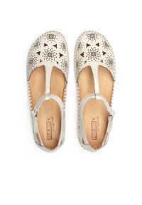 Sandales en cuir beige clair avec un design floral découpé, sangle T et boucle réglable à la cheville. Semelle plate avec une texture imitant le bois naturel.