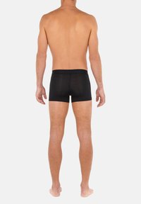 Schwarze Boxershorts aus elastischem Stoff mit glatter Textur und einfachem Bund, von hinten an einer nackten Figur gezeigt.