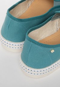 Teal textiele instap schoenen hebben een gestructureerde bovenkant, een crèmekleurige zool en gevlochten jute accenten met goudkleurige logo-details.