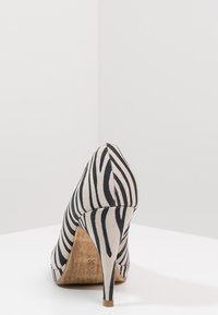 High-heeled shoe featuring a pointed toe and a zebra stripe pattern in black and beige fabric, with a wooden heel. Size displayed is 36.