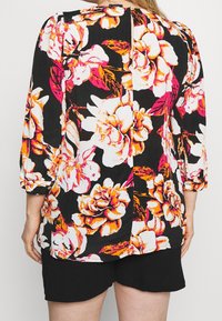Blusa nera a fiori con grandi fiori bianchi e rosa, maniche a tre quarti, scollo rotondo e orlo dritto. Tessuto testurizzato.