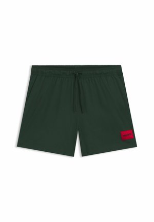 Costumi da bagno verde scuro con vita elastica e cordoncino. Presenta una toppa rettangolare rossa con il logo "HUGO" sul lato sinistro.