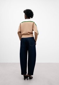 Maglione lavorato a maglia beige con accenti bianchi e verdi, abbinato a jeans a gamba larga blu scuro. Le scarpe con il tacco completano il look.