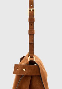 Borsa in suede marrone con un design strutturato. Presenta una tracolla removibile, hardware dorato e piping nero lungo i bordi.