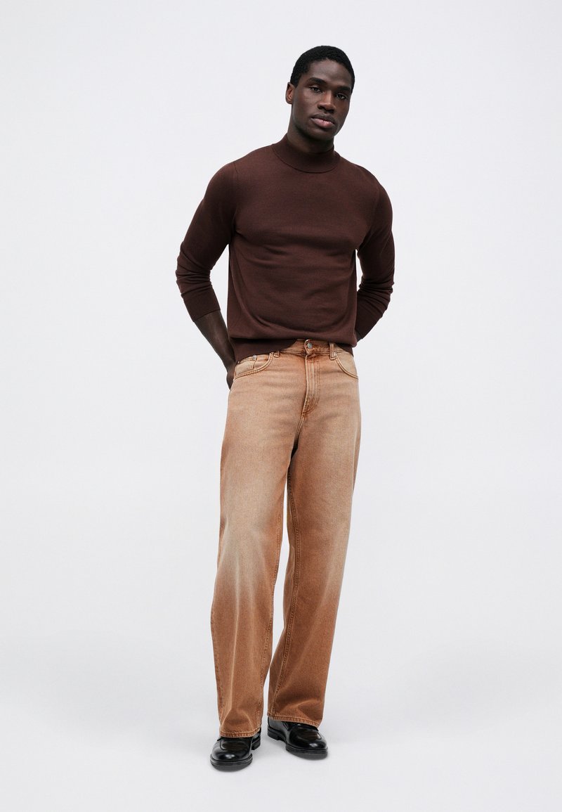 Brun strikket turtleneck-sweater parret med lysebrune brede denimbukser. Sorte lædersko fuldender outfittet. Enkel design, tætsiddende silhuet.