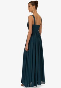 Langes tealfarbenes Abendkleid mit tailliertem Oberteil, gerafftem Rücken und breiten Trägern. Der Rock fließt und ist gerafft, was die Silhouette betont.