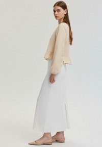Lichtbeige cropped blouse met ruches aan de onderkant, gecombineerd met een lange witte rok met een zijsplit. Gemaakt met nude slingback flats.