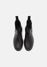 Botas negras de cuero hasta el tobillo con paneles laterales elásticos, tiradores y un acabado suave. Diseño minimalista con punta redondeada y suela plana.