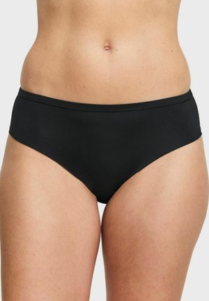 Vrouw die eenvoudige zwarte bikinibroekjes met een middelhoge taille draagt, getoond van taille tot bovenbenen tegen een effen lichte achtergrond.