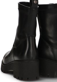Botas negras de cuero hasta el tobillo con una suela de goma gruesa, que presentan una textura suave y un detalle de cremallera en la parte posterior.