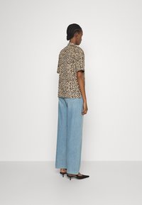 Camisa de manga curta com padrão de leopardo, combinada com jeans de perna larga de tom azul-claro e sapatos de salto agudo pretos. Tecido suave com um corte descontraído.