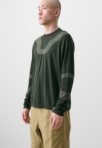 Long-sleeve dark green shirt with a textured design featuring patterned accents on the shoulders and sleeves.