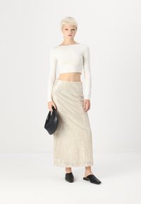 Dlhá strieborná sukňa s flitrami v úzkom strihu doplnená bielym crop topom s dlhým rukávom. Doplnky tvoria čierna kabelka a čierne topánky na slip-on.