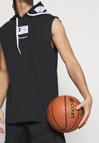 Black sleeveless hoodie with a white-lined hood and Champion logo. Holding a brown basketball with "all-court" branding.