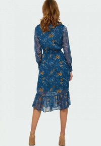 Robe longue florale en bleu avec des manches longues transparentes. Présente une taille cintrée et un ourlet en volants, ornée de motifs floraux orange et blancs.