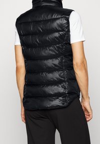 Czarna kamizelka puchowa z poziomymi przeszyciami, wysokim kołnierzem i bocznymi kieszeniami na zamek. Gładki, błyszczący materiał o dopasowanym kroju.