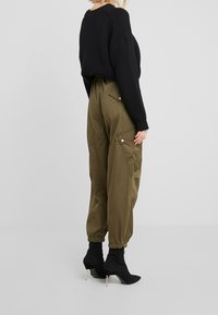 Zwarte geribde trui gecombineerd met olijfgroene cargo-broek met zijzakken en elastische boorden, aangevuld met aansluitende zwarte enkellaarsjes.