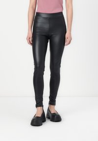 Black faux leather leggings with a high waist, form-fitting design, and a smooth, shiny texture. Paired with chunky black platform shoes.