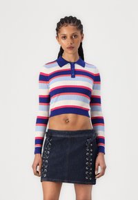 Pull cropped rayé avec des couleurs bleue, rouge et rose ; dispose d'un col et d'une patte de boutonnage. Jupe en denim foncé avec des détails à laçage sur les côtés.