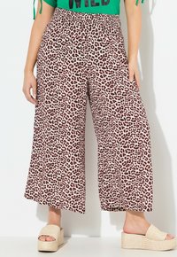 Weite Hosen in einem hellen Farbton mit einem schwarz-braunen Leopardenmuster; ausgestattet mit einem elastischen Bund und kombiniert mit einer geflochtenen Plateausandale.