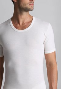 T-shirt bianco a maniche corte realizzato in un tessuto morbido e leggero. Presenta un collo rotondo e un design aderente, che mette in risalto la forma del torso.