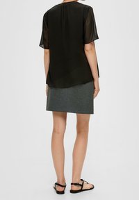 Haut noir transparent à manches courtes avec un col rond, porté sur une jupe cintrée grise. La tenue est complétée par des sandales plates noires.