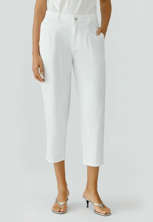 Weiße, gekürzte Hosen mit vorderen Falten, Knopf- und Reißverschluss, Seitentaschen, getragen mit einem weißen Oberteil und silbernen, offenen Absatzschuhen.