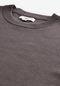 Pull en taupe foncé, avec un col rond côtelé. La texture est tricotée avec un tissu léger et doux, affichant un motif subtil.
