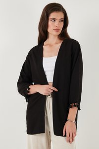 Chaqueta negra de estilo kimono con mangas tres cuartos, con decoración de encaje en los puños y un corte relajado. Se lleva sobre una blusa blanca.