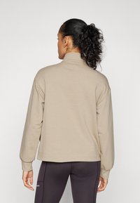 Beige, lange mouw sweatshirt met een hoge kraag en verlaagde schouders, met een gladde textuur en een relaxte pasvorm, gedragen met donkere leggings.
