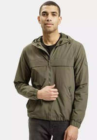 Zielona, lekka kurtka z kapturem, z suwakiem, elastycznymi mankietami oraz kieszonką na piersi. Nosi się ją na czarnej koszuli.