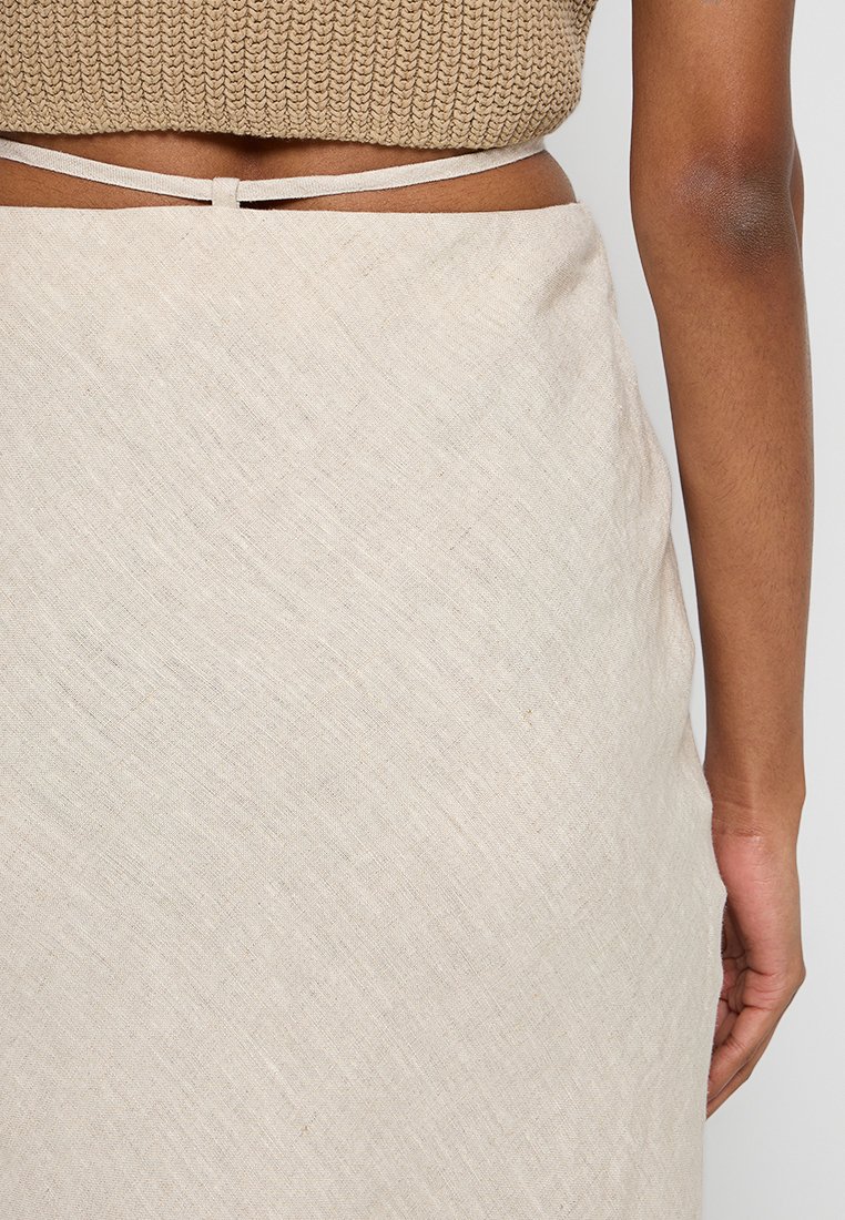 Helles beiges Kleid aus einem strukturierten Stoff. Verfügt über einen Krawattenbund und diagonale Webmuster für zusätzliche Details. Glatte, fließende Silhouette.
