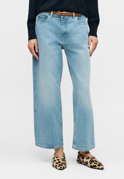 Jean large bleu clair avec une finition délavée, doté d'une fermeture bouton et fermeture éclair, cinq poches, et une ceinture marron.