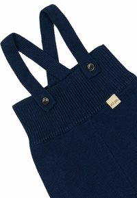 Strickoverall in Marineblau mit gekreuzten Schulterträgern, gerippter Textur und Knopfdetails. Mit einem kleinen Markenschild auf der Vorderseite.
