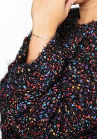 Texturerad svart tröja med multicolerade prickar i röd, blå, orange och lila. Löst snitt med synliga ärmar och manschetter.