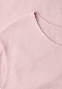 Tissu rose doux montrant un gros plan d'un col arrondi et des détails de couture sur un vêtement en coton lisse.