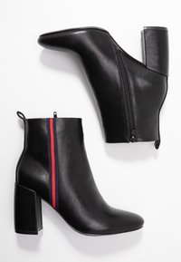 Bottes chevilles en cuir noir avec talons carrés, fermeture éclair latérale et détail de rayures verticales rouges et bleu marine sur le côté extérieur.