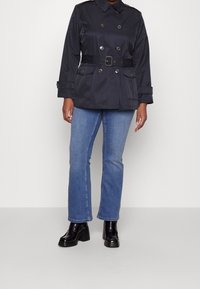 Chaqueta marinera de doble botonadura con cinturón en la cintura, dos bolsillos frontales y botones plateados. Combinada con jeans azul claro y zapatos de plataforma negros.