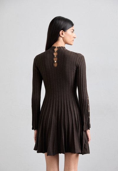 Robe en tricot côtelé marron avec des manches longues, une jupe évasée et des accents de boutons à l'arrière. La texture est extensible et ajustée.