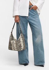 Sac hobo en cuir simulé imprimé serpent beige et noir, avec une forme douce, une surface texturée et une seule sangle courbée. Associé à un jean bleu clair.