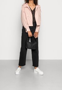 Giacca impermeabile rosa chiaro con cappuccio, top nero a fantasia, jeans neri larghi e sneakers bianche con zeppa. Tiene una piccola borsa nera.