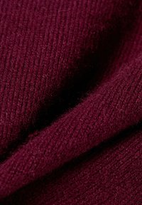 Bordeauxfarbener Strickstoff mit einer gerippten Textur, zeigt weiche Fasern und ein leicht flauschiges Aussehen. Geschmeidiger Fall mit einem warmen Ton.