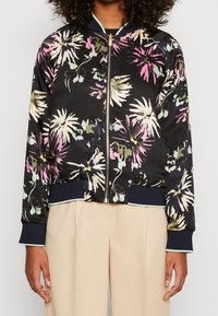 Zwarte bomberjack met een bloemmotief in roze, groen en wit. Het heeft een ritssluiting aan de voorkant, geribde manchetten en een zoom met contrasterende afwerking.