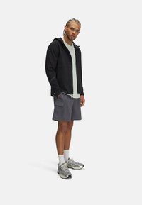 Mustmiliseg sweatshirt, millel on tekstuurne muster, heledad hallid T-särk, tumehallid lühikesed püksid ja hallid spordijalatsid. Seisev poos, käed taskus.
