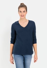 Marineblauwe V-hals trui met lange mouwen, textuur gebreide stof, ontspannen pasvorm, gecombineerd met lichtblauwe jeans.