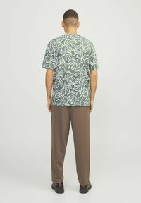 Korte mouwen groene t-shirt met een wit bladdessin, gemaakt van lichtgewicht stof, gecombineerd met een bruine broek en zwarte schoenen.