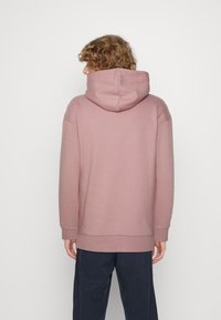Roze hoodie met een relaxte pasvorm en lange mouwen. Heeft ribgebreide manchetten en gelikte zoom, een zachte textuur en een kangoeroezak.
