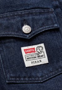 Levi's traper jakna s kopčanjem na dugmad, tamnoplave tkanine i oznakom koja prikazuje "AUTENTIČNA WESTERN ODEĆA" s Pixar grafikom.