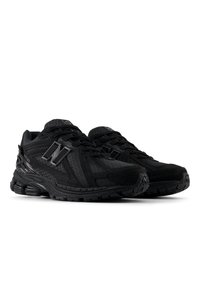 Paire de chaussures de running New Balance entièrement noires avec semelles rembourrées, empeignes en mesh et synthétique, et détails du logo sur les côtés et la languette.